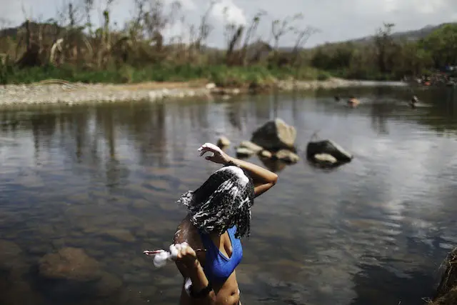 A woman washes her hair in the Espiritu Santo river, along hurricane-damaged forest, more than two weeks after Hurricane Maria hit the island, on October 8, 2017 in Palmer, Puerto Rico.